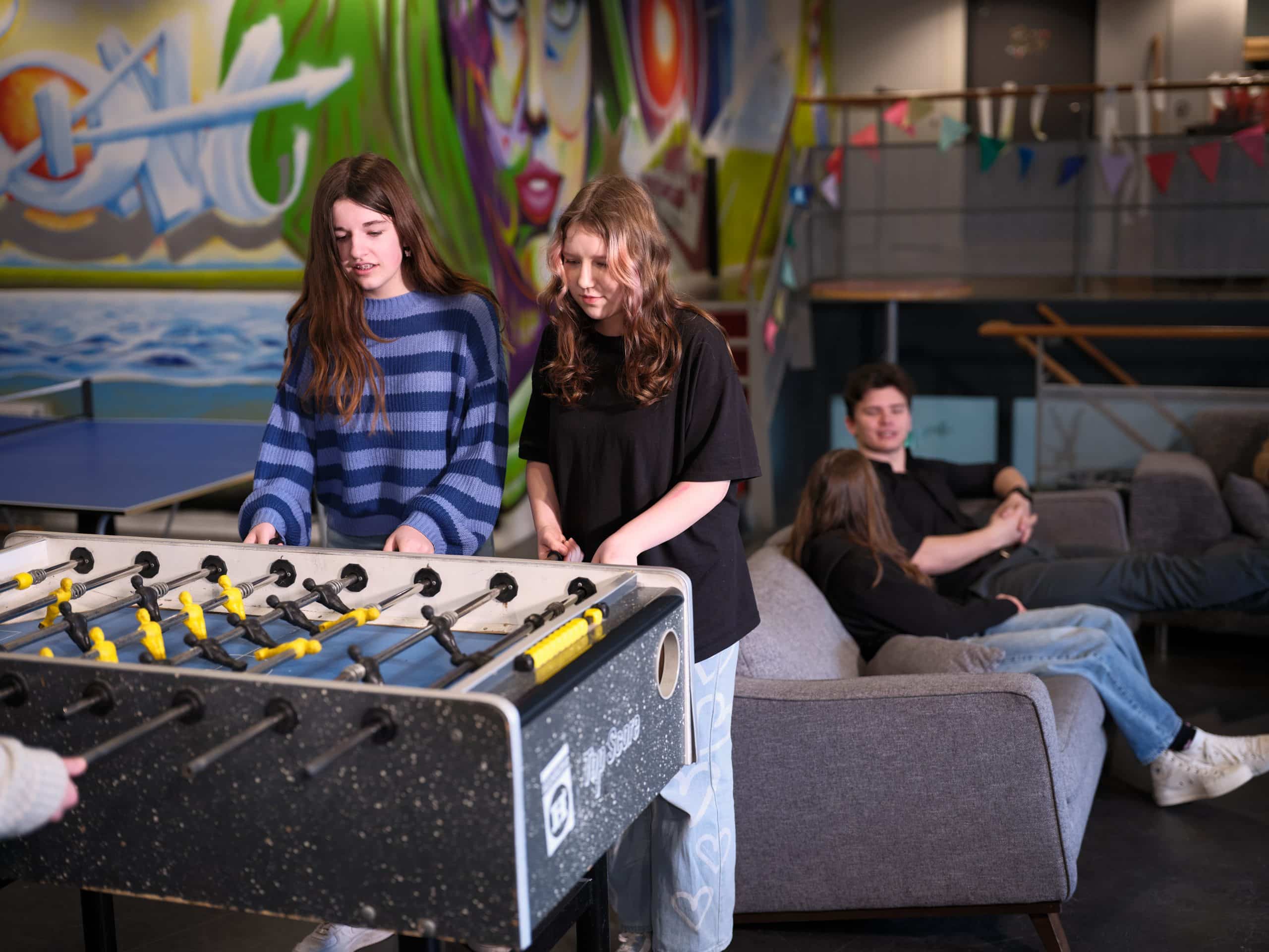 Jongeren die samen spelen aan tafelvoetbaltafel en jongere die op bank zit